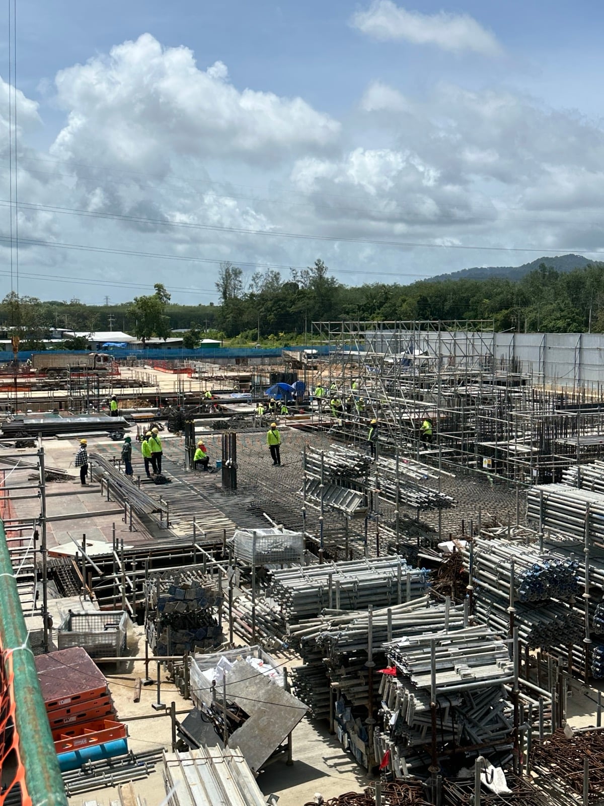 Workers laying reinforcement mesh beside stacked scaffolding materials